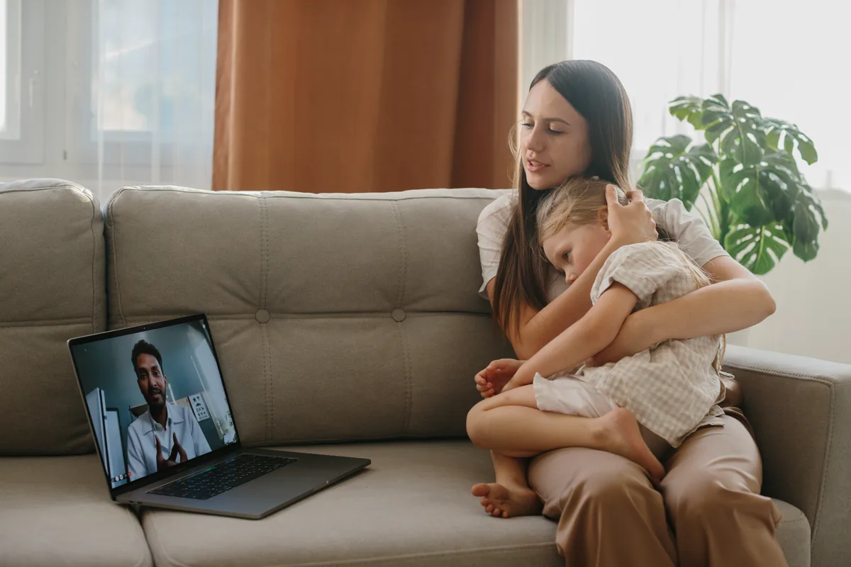Parent and child sitting at home with a laptop nearby for a pediatric telehealth visit.