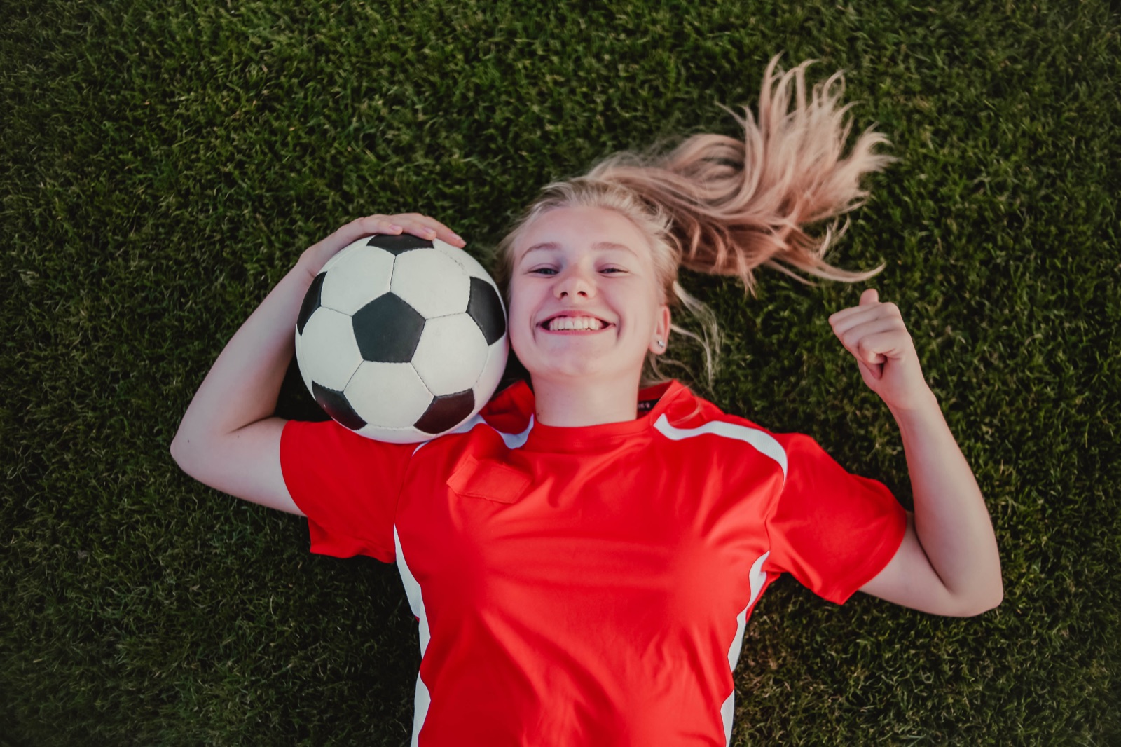 Smiling young soccer player lying on grass with a soccer ball.